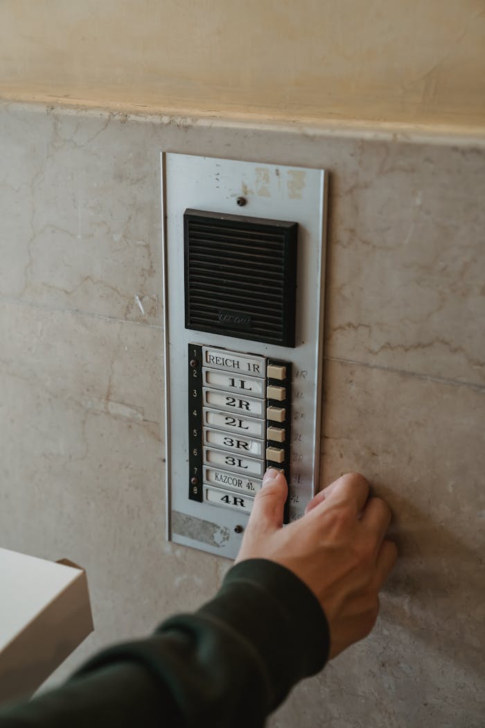 Close-up of a hand pressing an intercom button outdoors on a building wall.